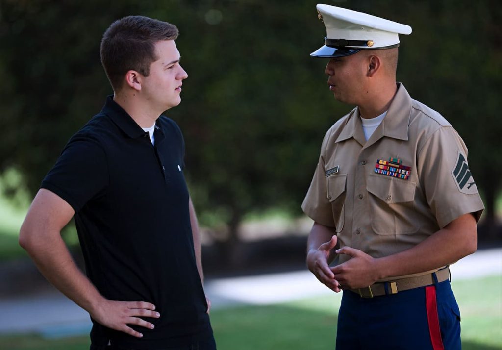 Marine talking to a civilian, with trees and grass in the background.